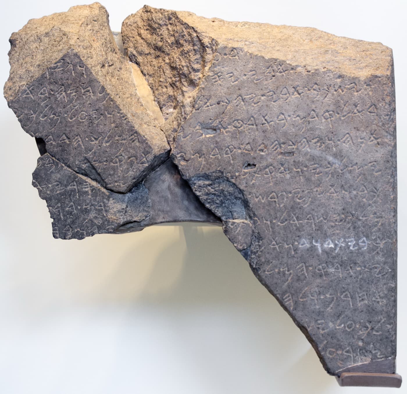 Three joined fragments of a black basalt stone carved with lines of ancient Aramaic letters